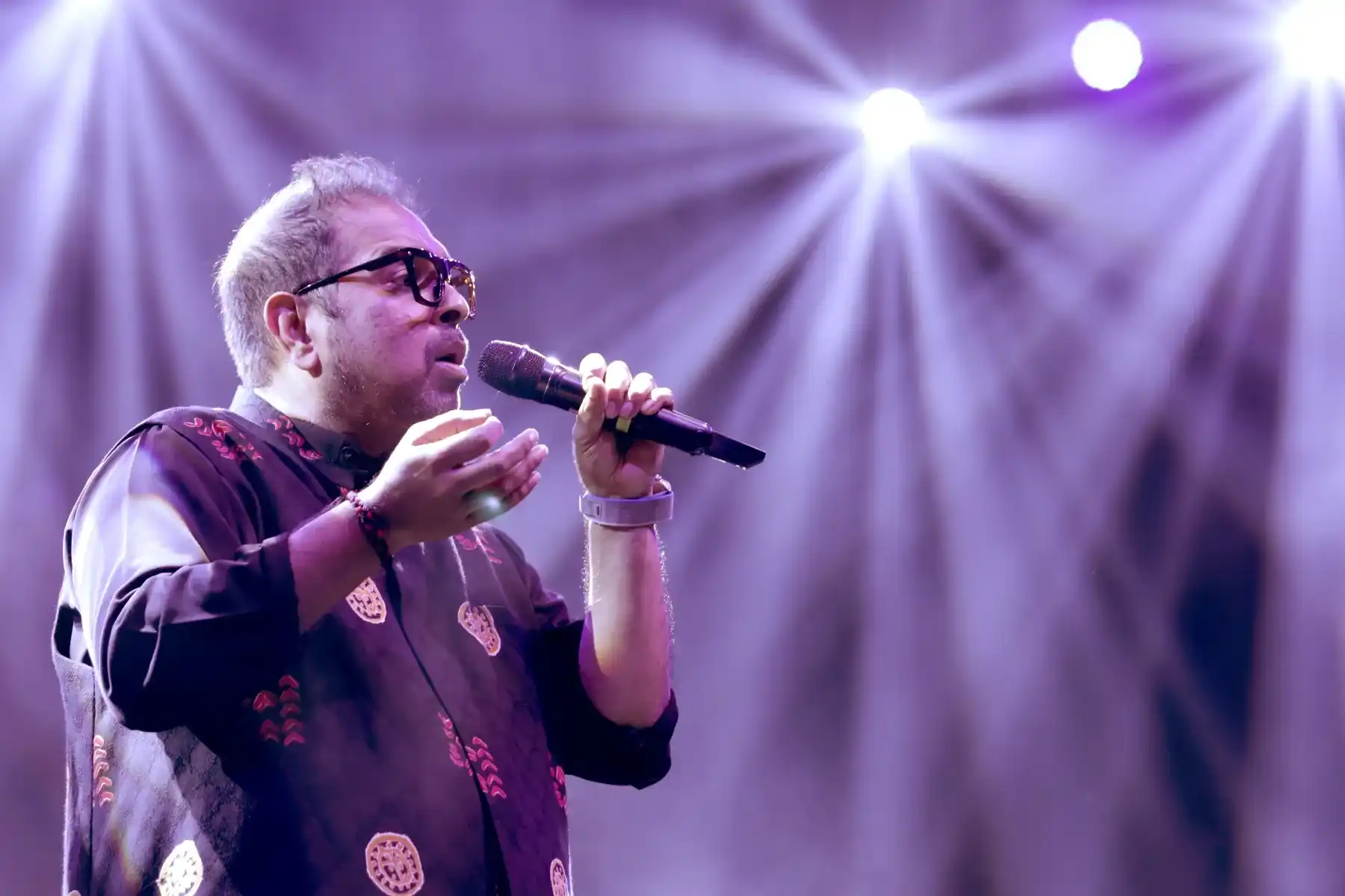 A vocalist performing live under purple stage lighting