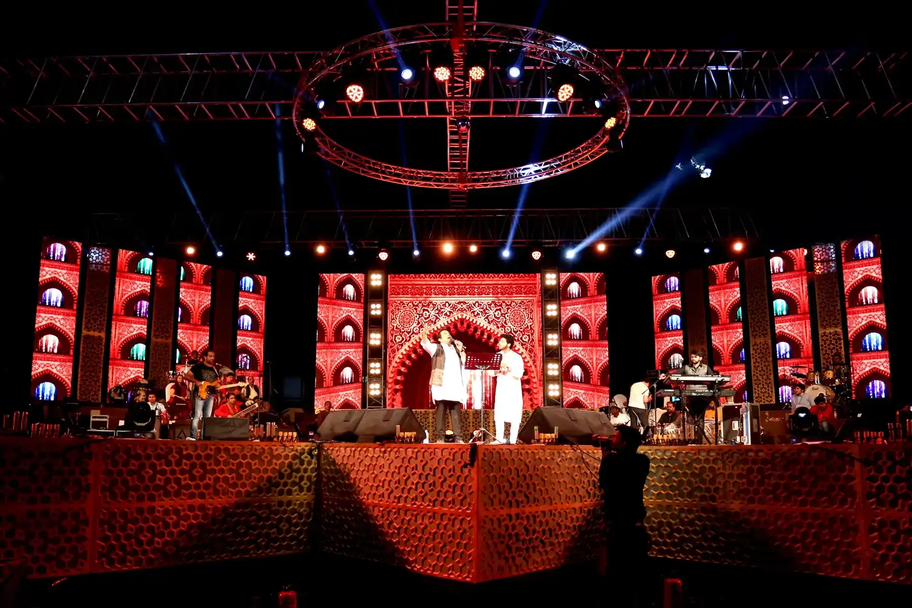 Performers on a large festival stage with an ornate lit backdrop