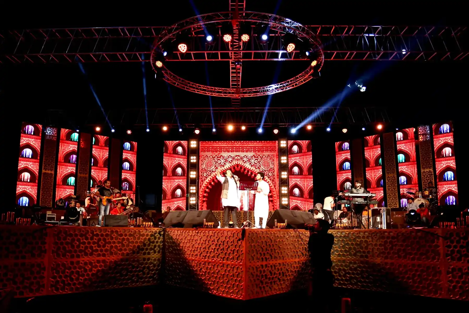 Performers on a large festival stage with an ornate lit backdrop
