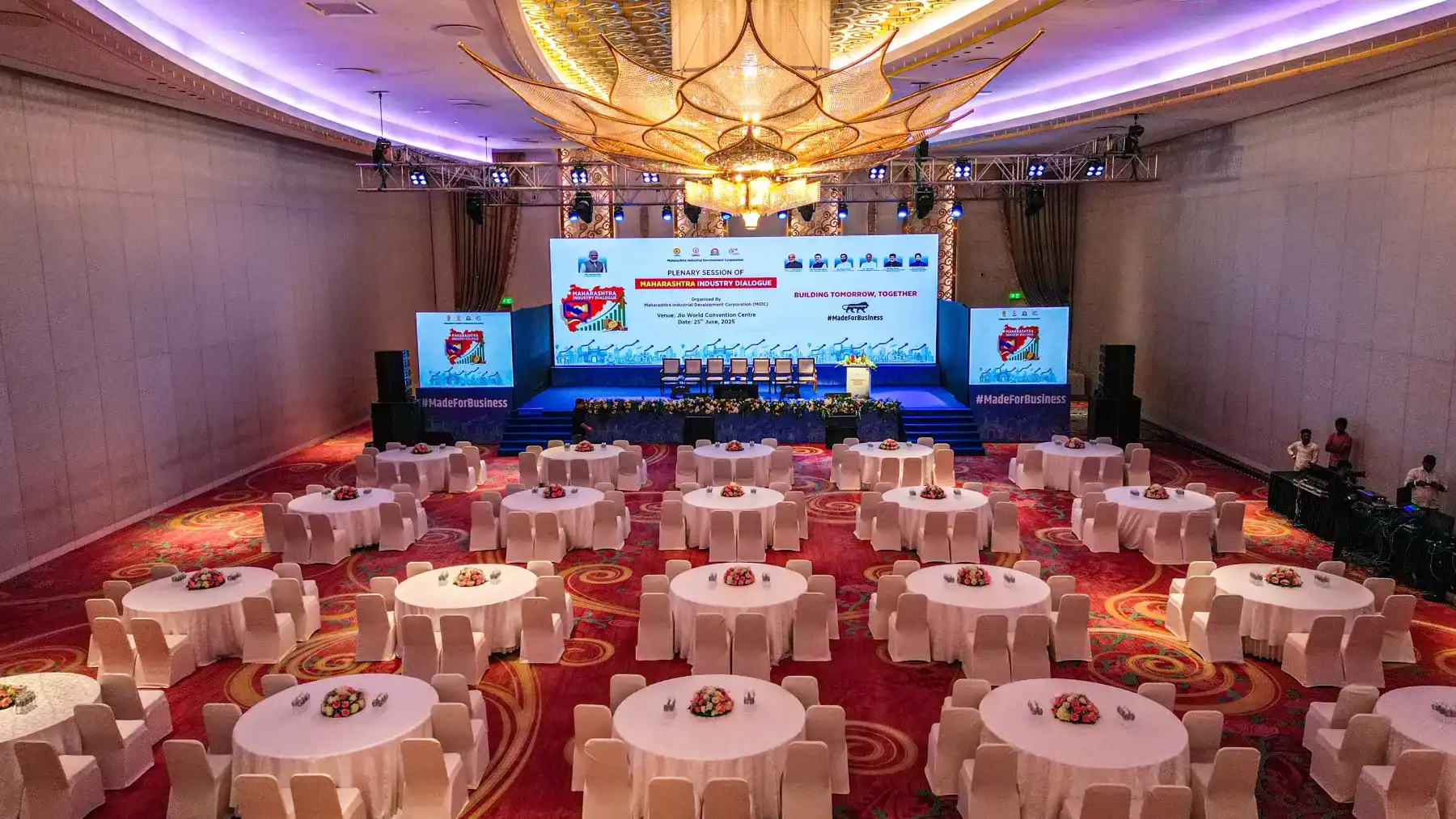 A grand banquet hall set with round tables facing a branded stage