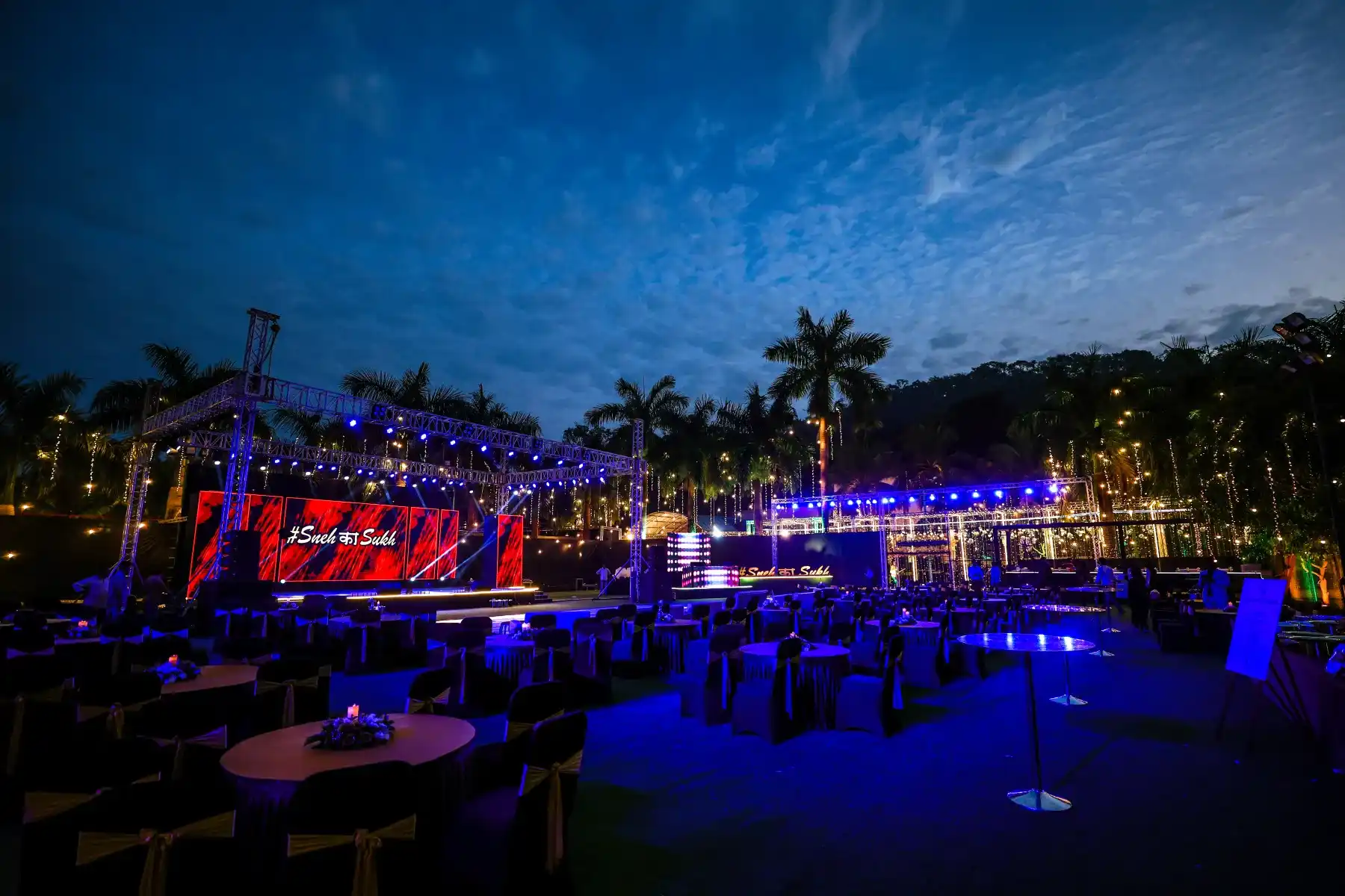 An outdoor evening wedding stage lit in blue with an LED screen