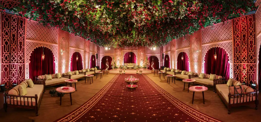 An ornate indoor wedding mandap with a floral ceiling, lounges and a red carpet