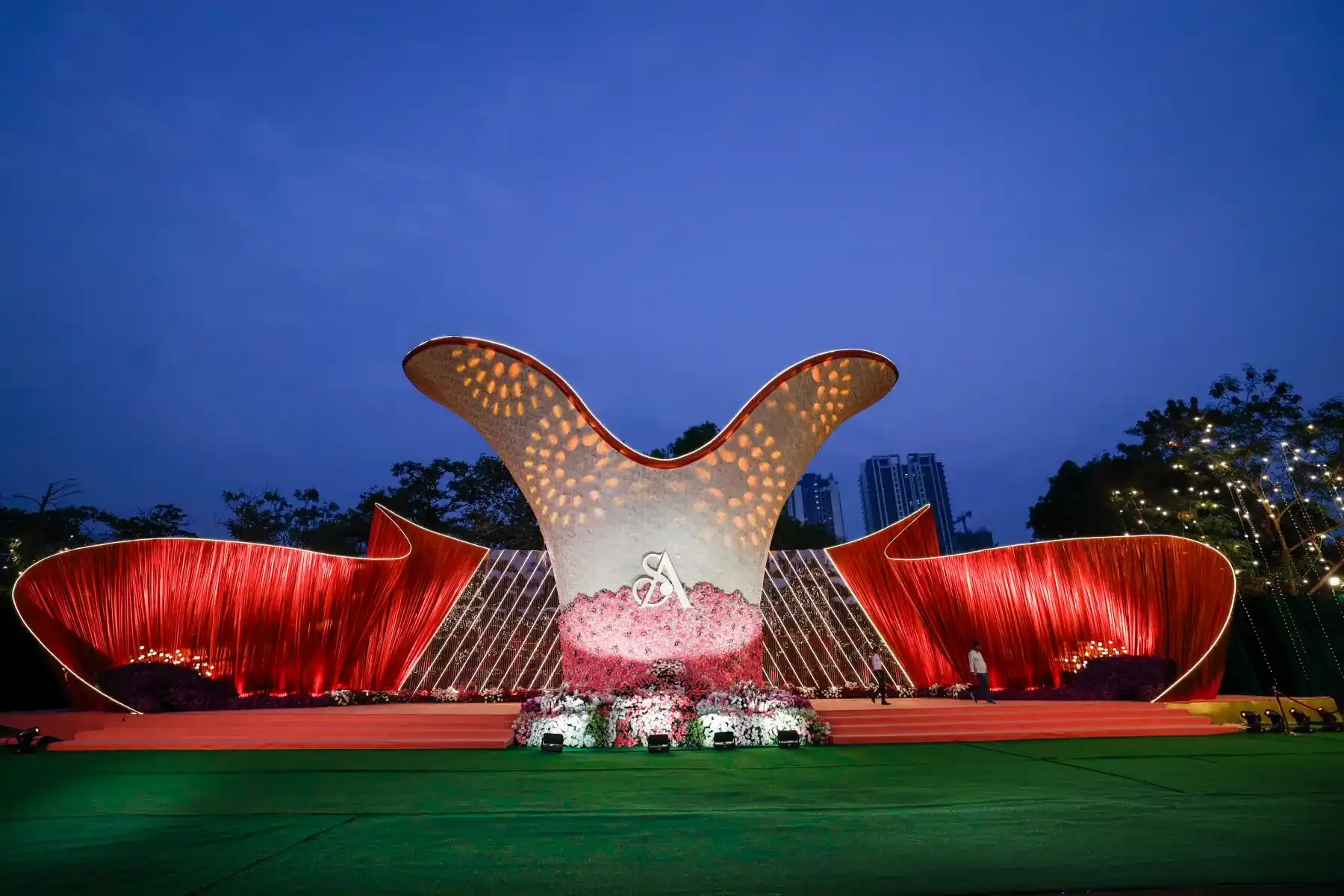 A dramatic sculpted wedding stage with red drapes against an evening sky