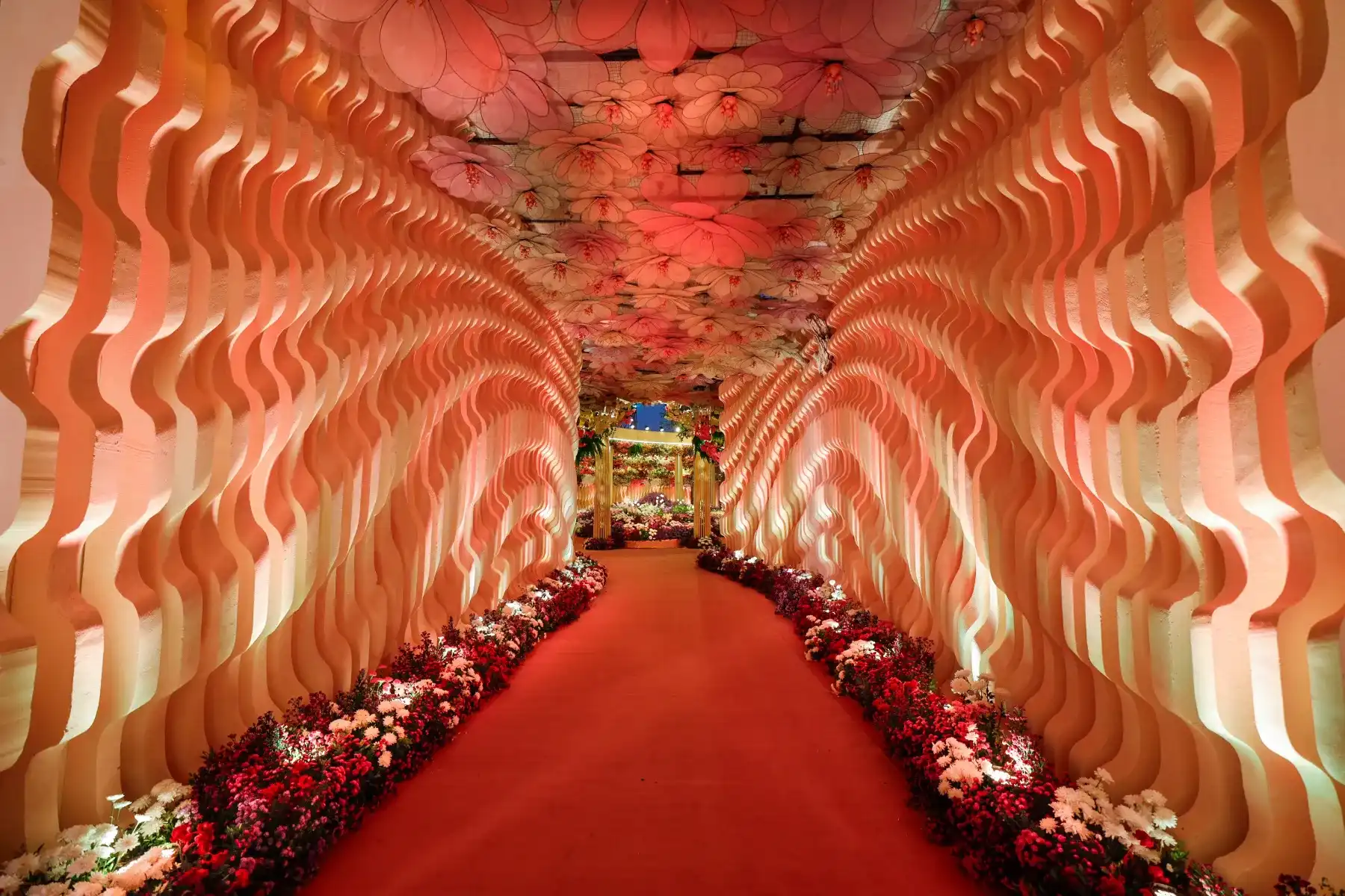 A flower-lined walkway framed by sculpted, warm-lit drapes